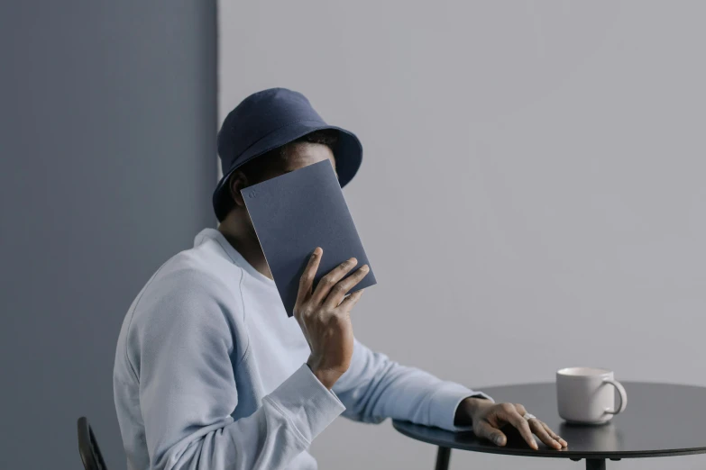 a man in a hat holding a book over his face