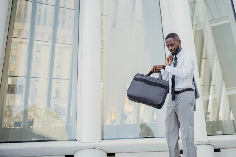 a man standing outside with his suit case on a cell phone