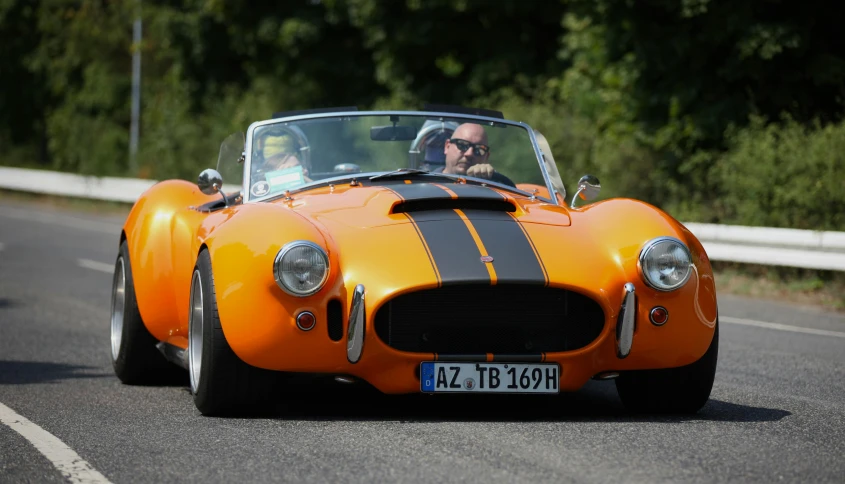 the front of an orange sports car being driven by a man