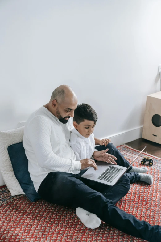 father and son sitting on the floor working on a laptop