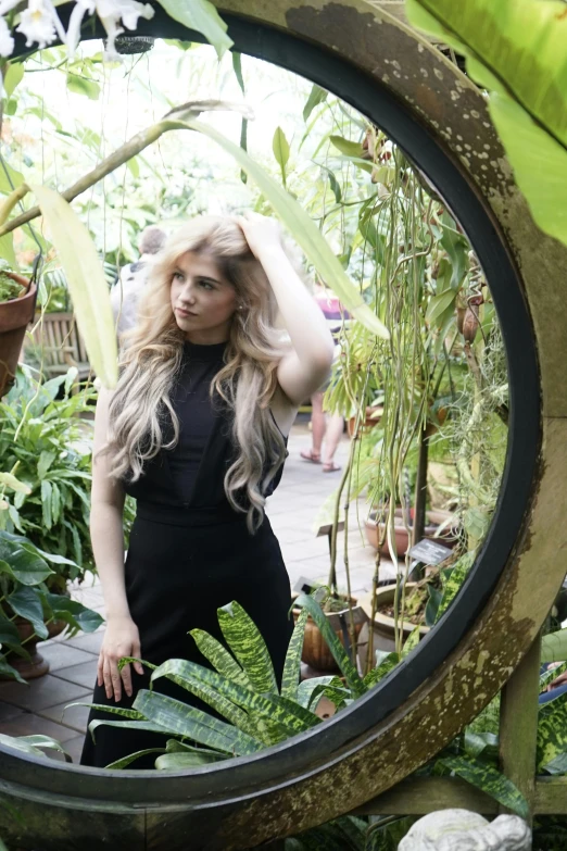 a woman in black jumpsuit standing next to a plant filled garden