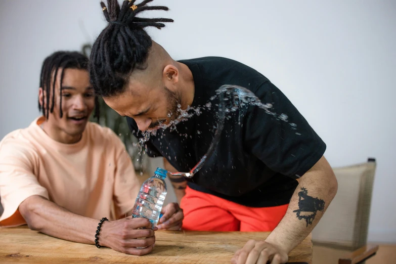 two men sitting at a table, one holding a water bottle