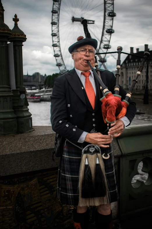 a man wearing a kilt holding a pipe by the london eye