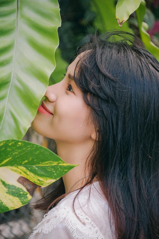 a young lady holding onto large green leaf