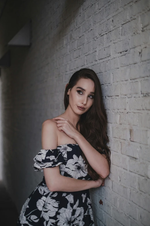 the beautiful woman is leaning against a white brick wall