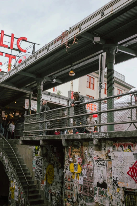 people walking underneath a pedestrian bridge covered in graffiti