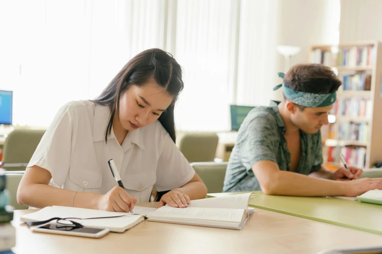 a girl sits at a table while a boy sits at her desk with books and textbooks