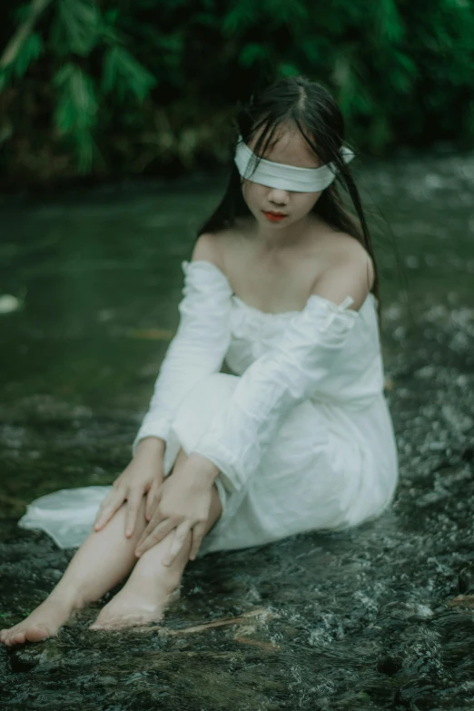 a girl in white shirt sitting on ground near water