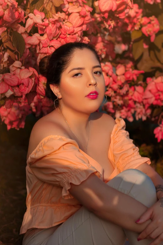 a beautiful woman wearing an off shoulder dress sitting under a flowery tree