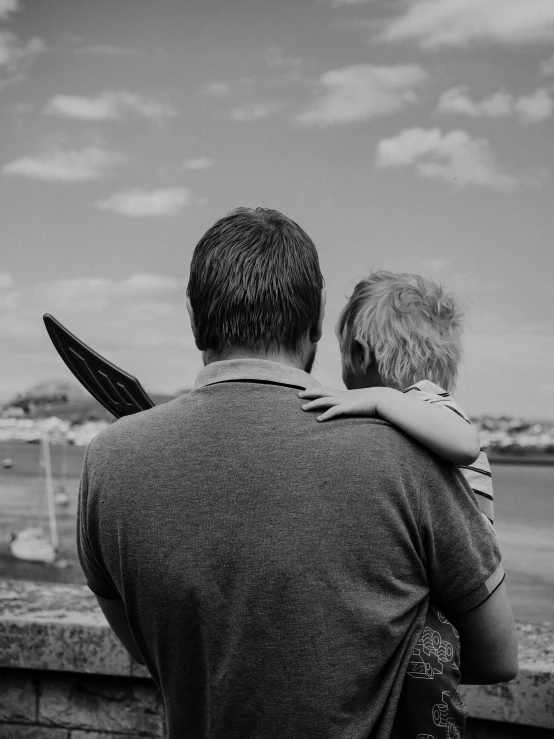 a boy and an adult hug while standing on a railing by the water