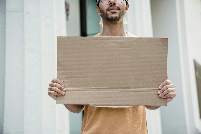 a young man in glasses holding up a cardboard board