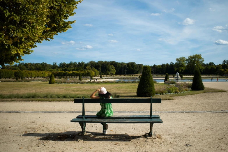 the person in the hat is sitting on a bench looking out over a garden