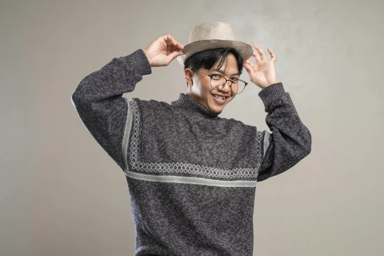 a man in a black sweater, hat and glasses standing with his hands on the ears