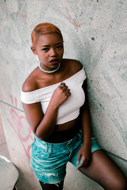 an attractive woman leaning against the wall wearing a belt and some shorts