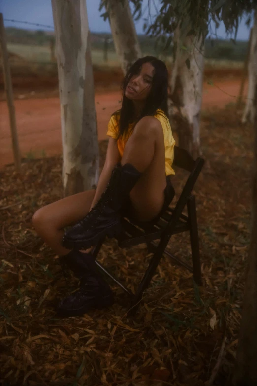 a woman wearing a yellow shirt sitting on a black chair next to some trees