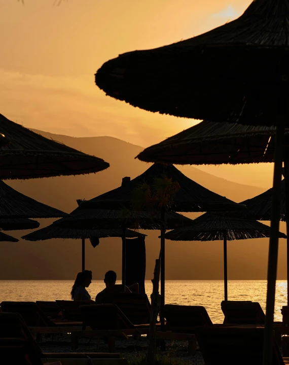 people are sitting in umbrellas at sunset by the ocean