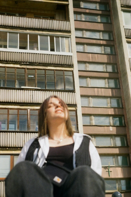 a young person sitting on the ground next to some tall building