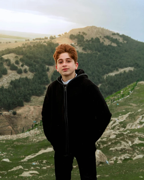 a boy in a hoodie standing on top of a hill