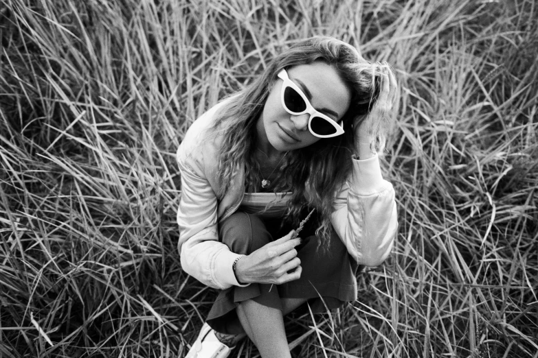 a woman sitting in tall grass holding a camera