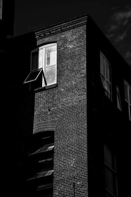 the corner of an old brick building with a window with a light shining in it