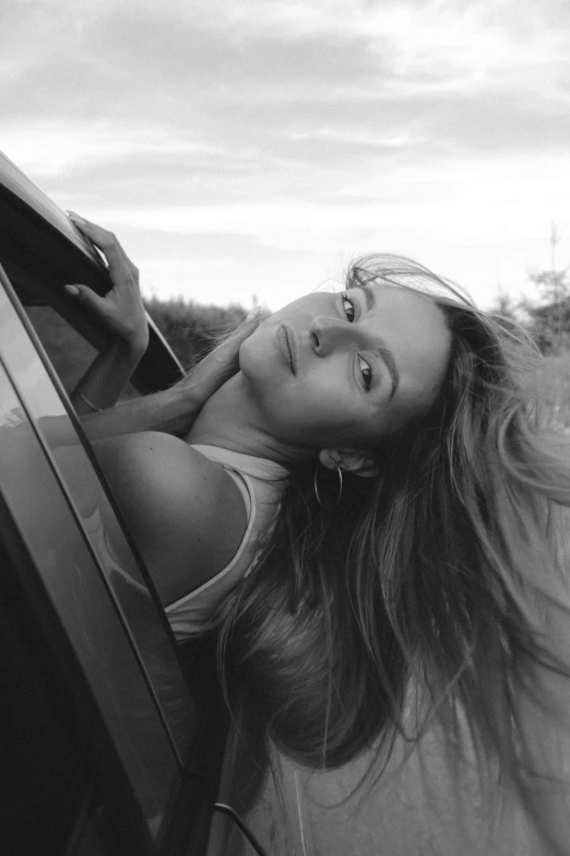 a black and white pograph of a woman with headphones leaning out the window of a car