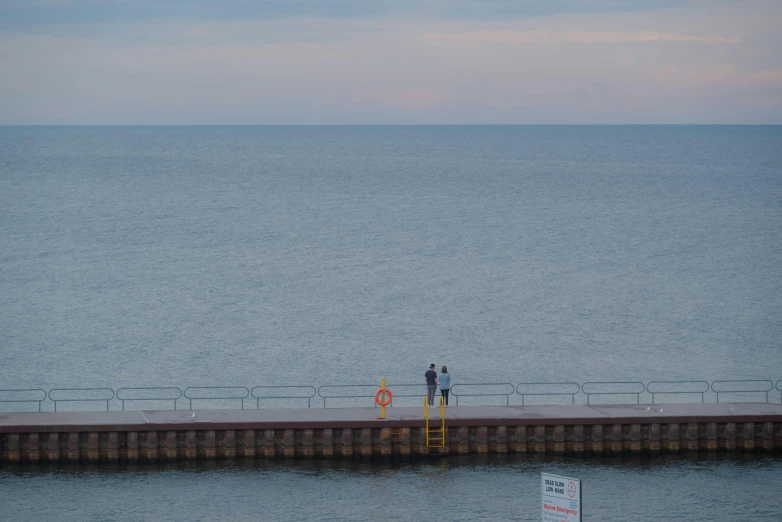 some people standing at the edge of the water by a pier