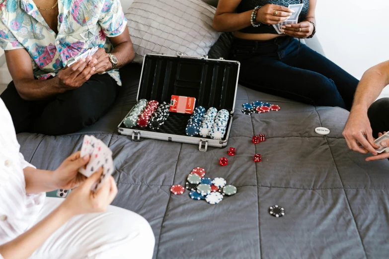 four ladies sit on a bed next to a suitcase with cards and chips