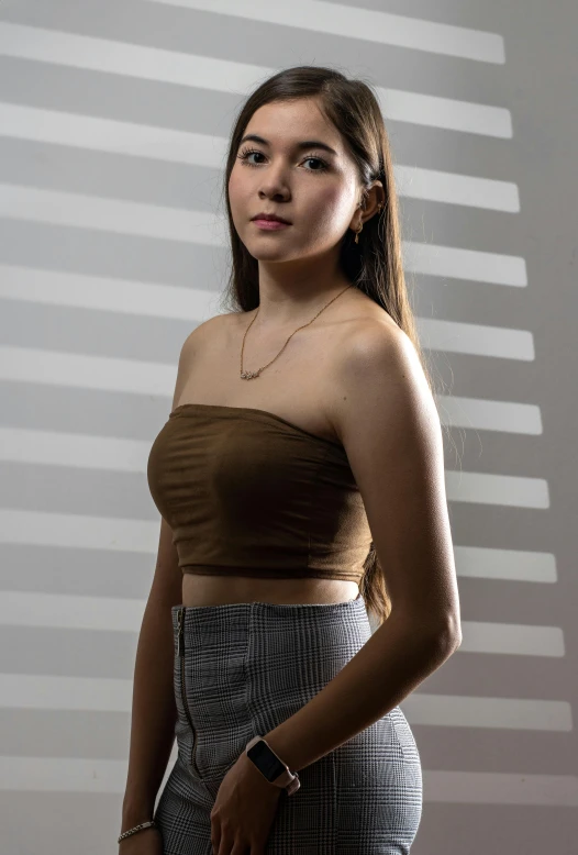 a woman in a brown top standing against a wall