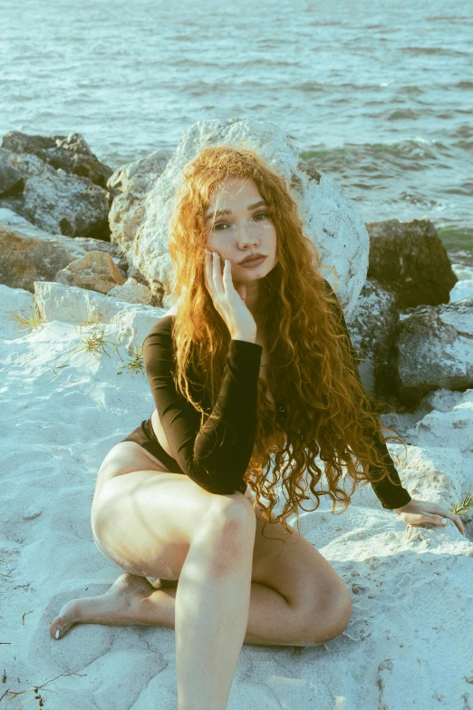 an attractive young woman sitting on the snow by the water