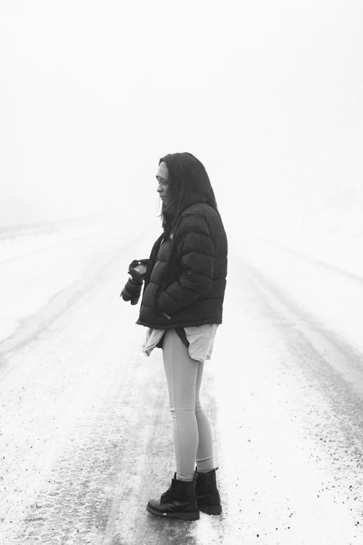 a woman in a coat is standing alone on a road