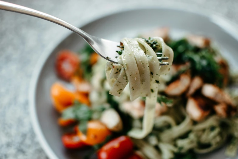 fork taking spaghetti with vegetables and herbs from a white bowl