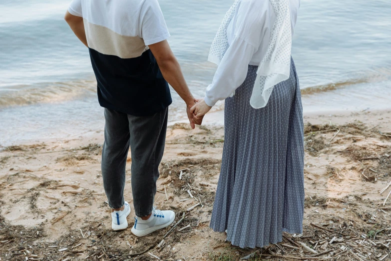 an older couple holds hands as they stand on the beach