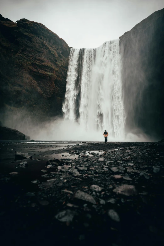 the lone figure is standing at the base of the waterfall