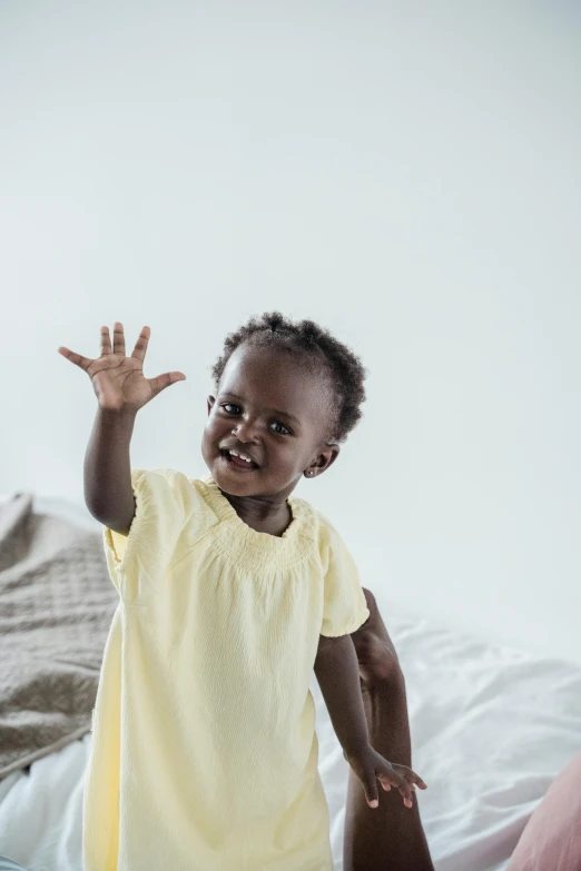 an adorable child waving and sitting on a bed