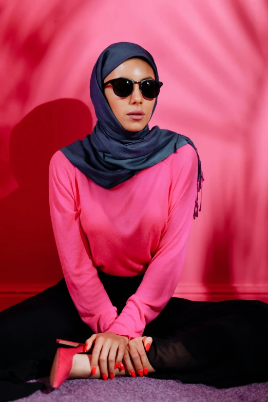 a woman is wearing a hijab and sunglasses sitting on the floor