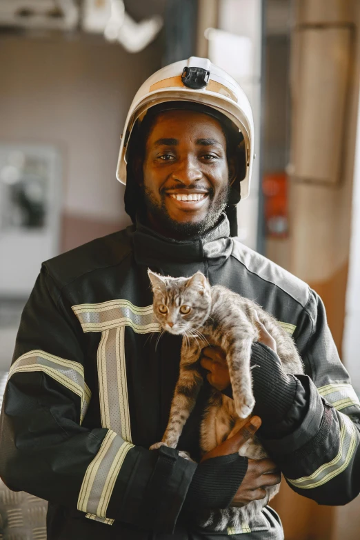 a smiling fireman in black jacket holding a cat