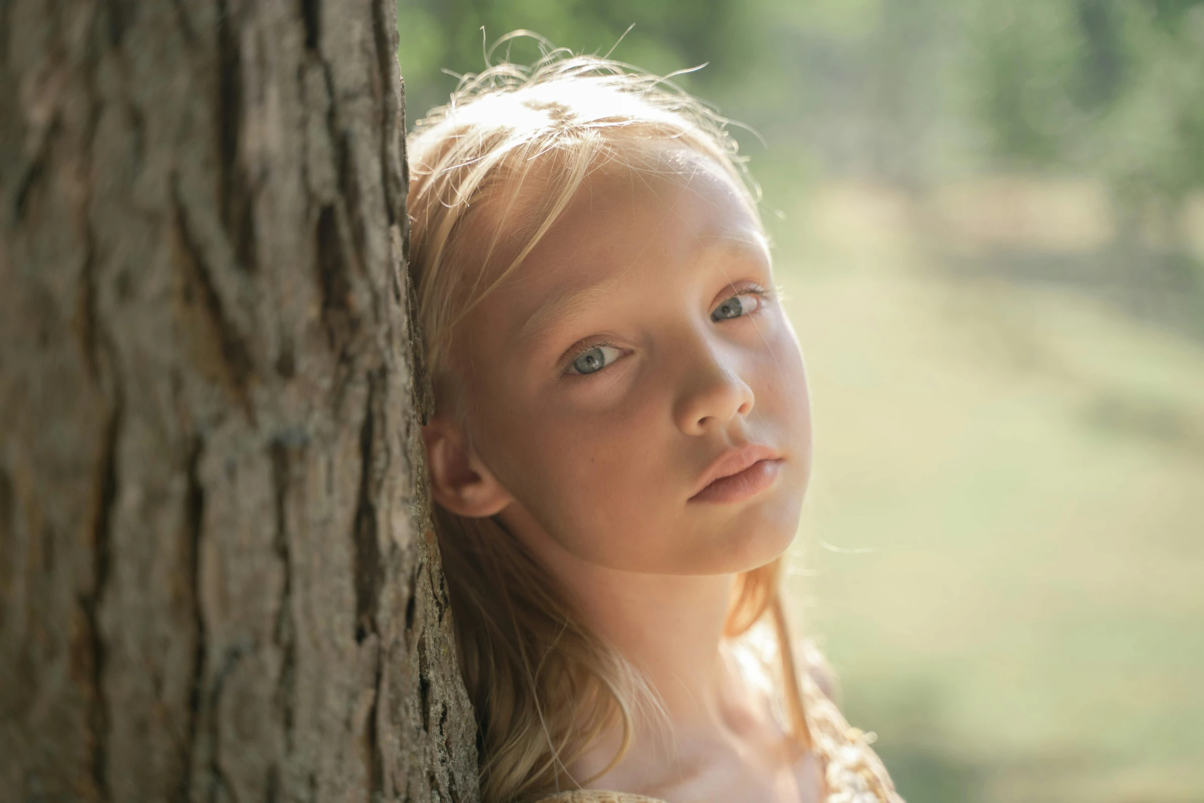 a little girl is peeking out from behind a tree