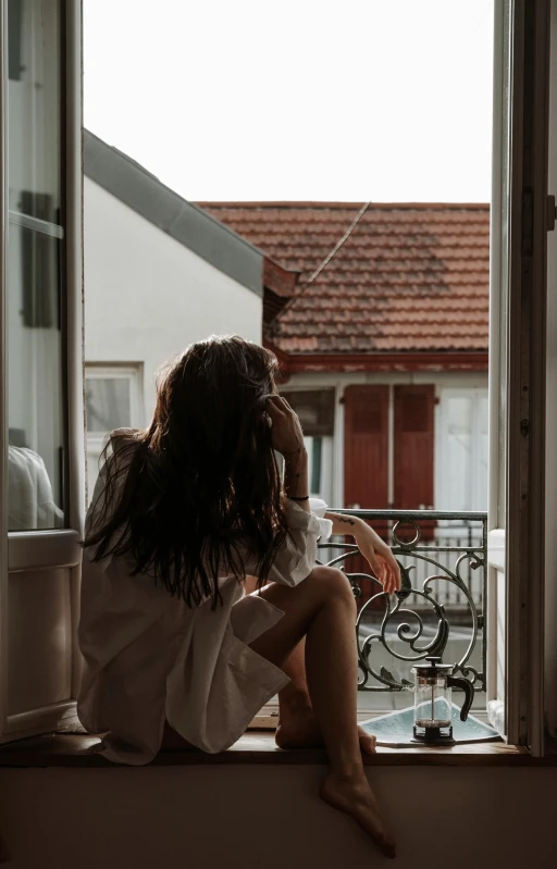 a woman sitting on the window sill looking out of a window