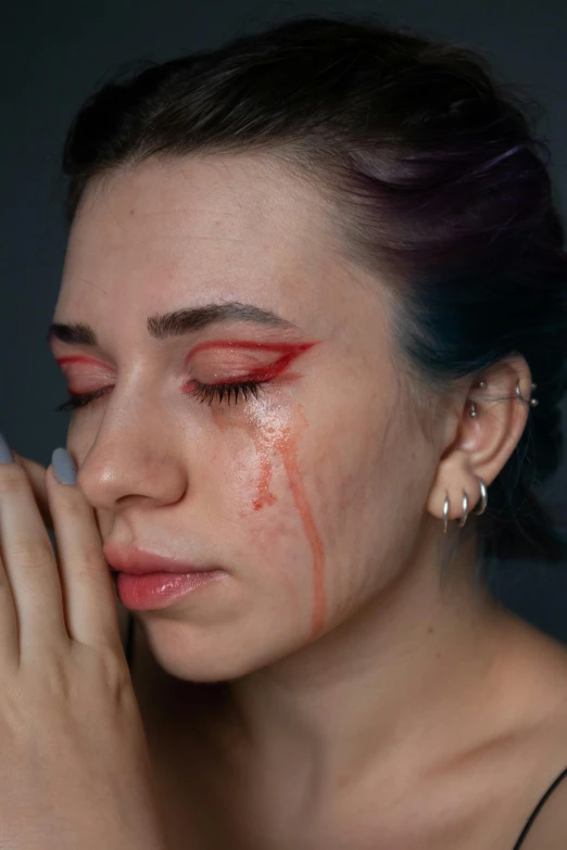 a woman with red make up holding her face in the dark