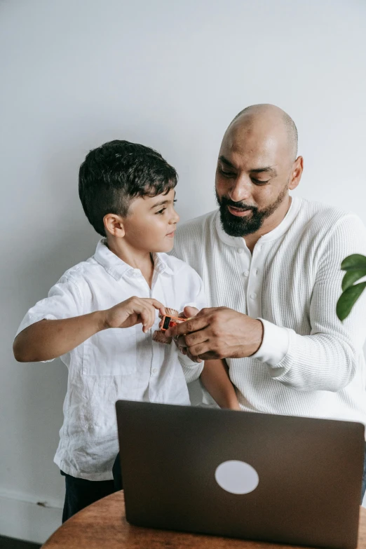 a man sitting at a desk with a boy who is looking at his laptop