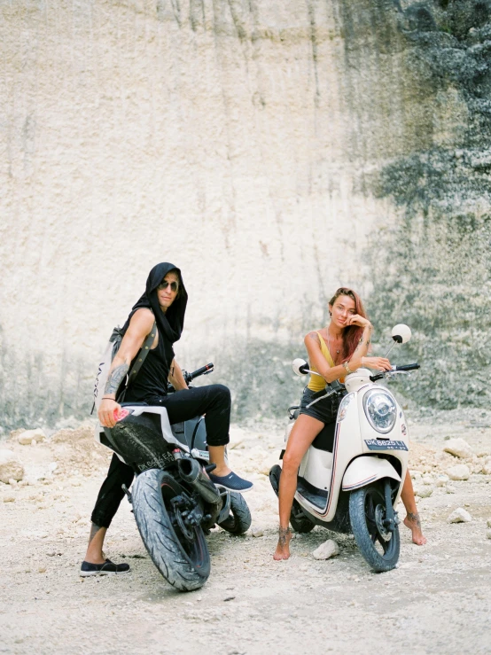 two people are on motor scooters in front of a stone wall