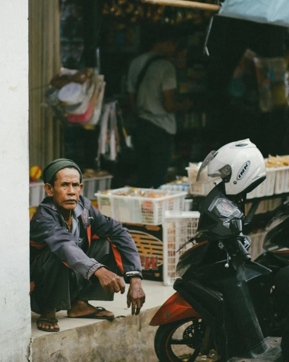 man sits at the edge of a sidewalk near his motorcycle