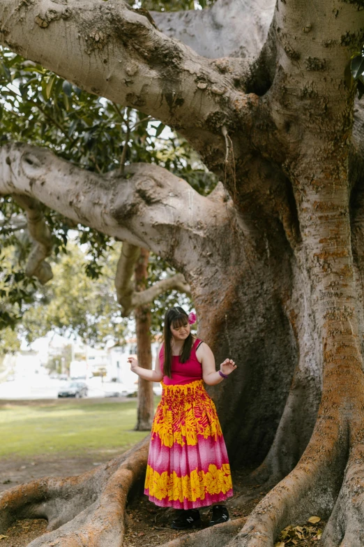 a girl in a red and yellow dress standing next to a tree