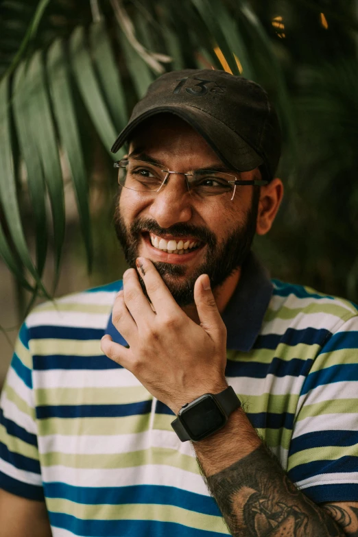 the man with a watch is smiling and leaning against a palm tree