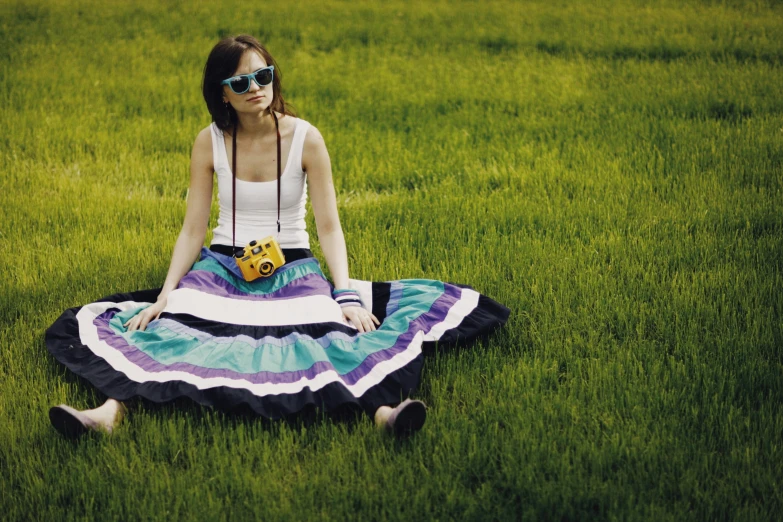 a woman in sunglasses sitting on grass with a flower in her hair