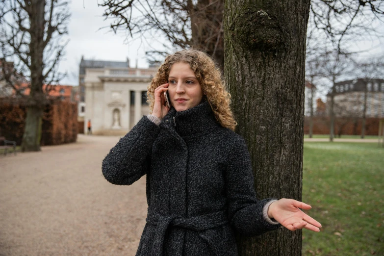 a woman is standing by a tree talking on her phone