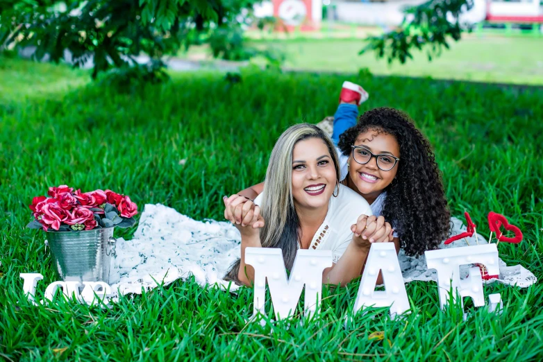 two women laying in the grass with a paper sign that says i love you