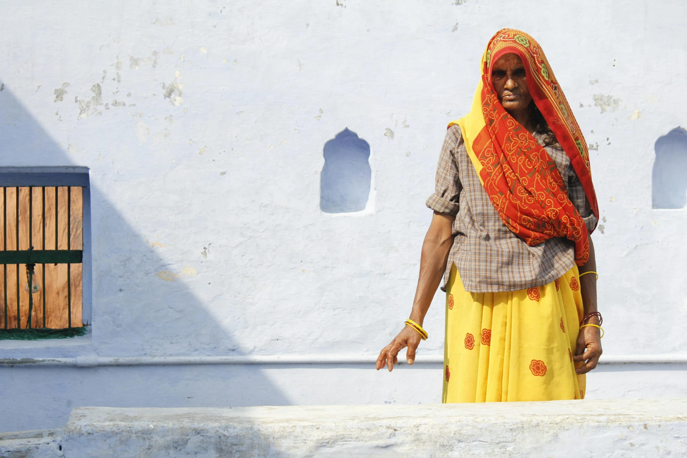 a woman in yellow stands against a white wall