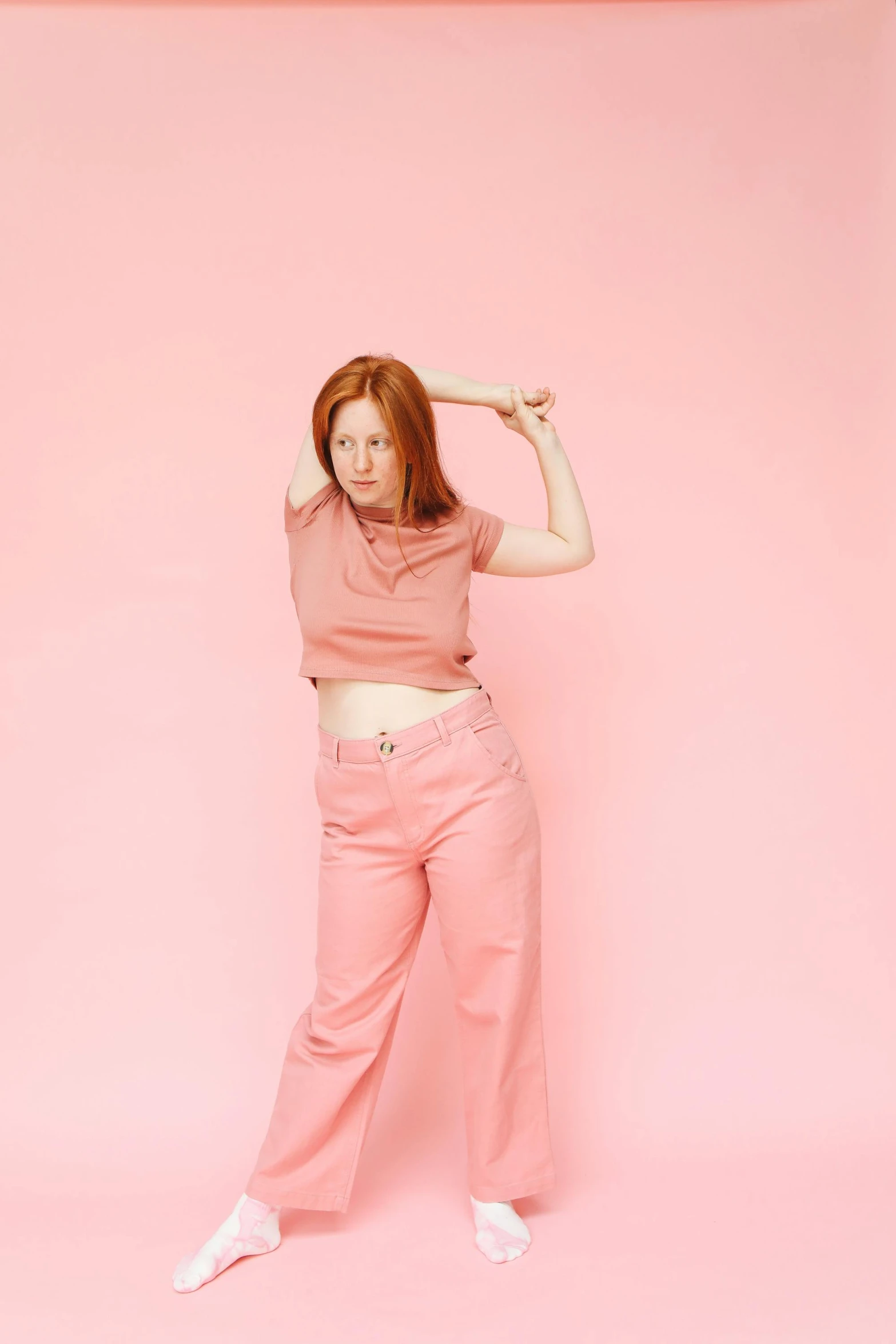 the woman with her hand on her head and in a pink top stands on a pink background