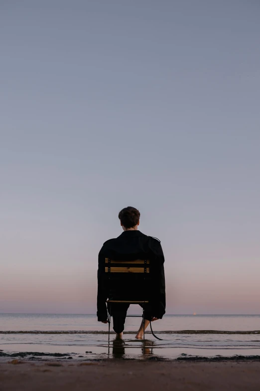 a man is sitting on a chair and looking out at the ocean